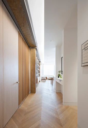 Entrance corridor, with custom oak wood paneling, chevron pattern wood flooring. Soft, indirect light emitting light cove in ceiling along corridor.