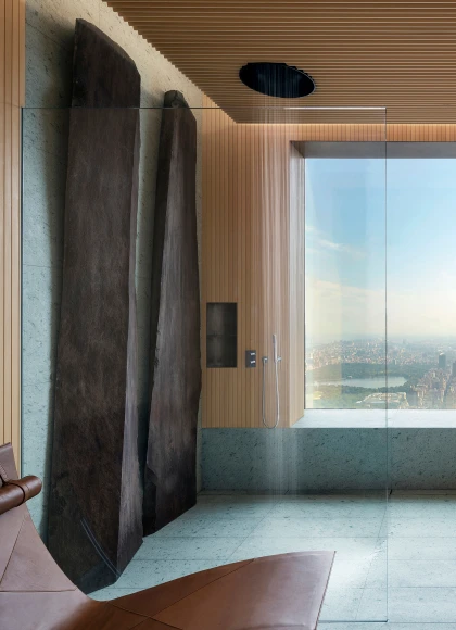 View of rain shower, with cedar wood slat clad walls and ceilings, green tuff stone clad floor, and two monumental granite stones leaning against the shower wall.