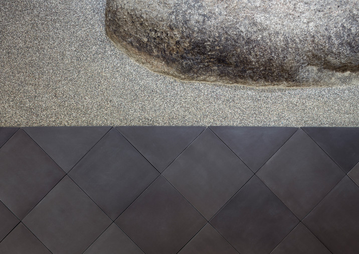 Floor detail of art niche in main corridor, with large boulder embedded in texted concrete. Bordered by handmade dark gray floor tiling, manufactured in Nara, Japan.