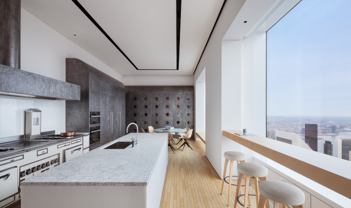 Kitchen view of stone countertop island, with custom furniture breakfast area in background and bar stool seating in front of window overlooking Midtown Manhattan.