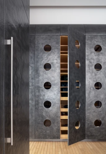 Detail view of hammered aluminum-clad kitchen cabinetry with round glass windows. Chestnut floors.